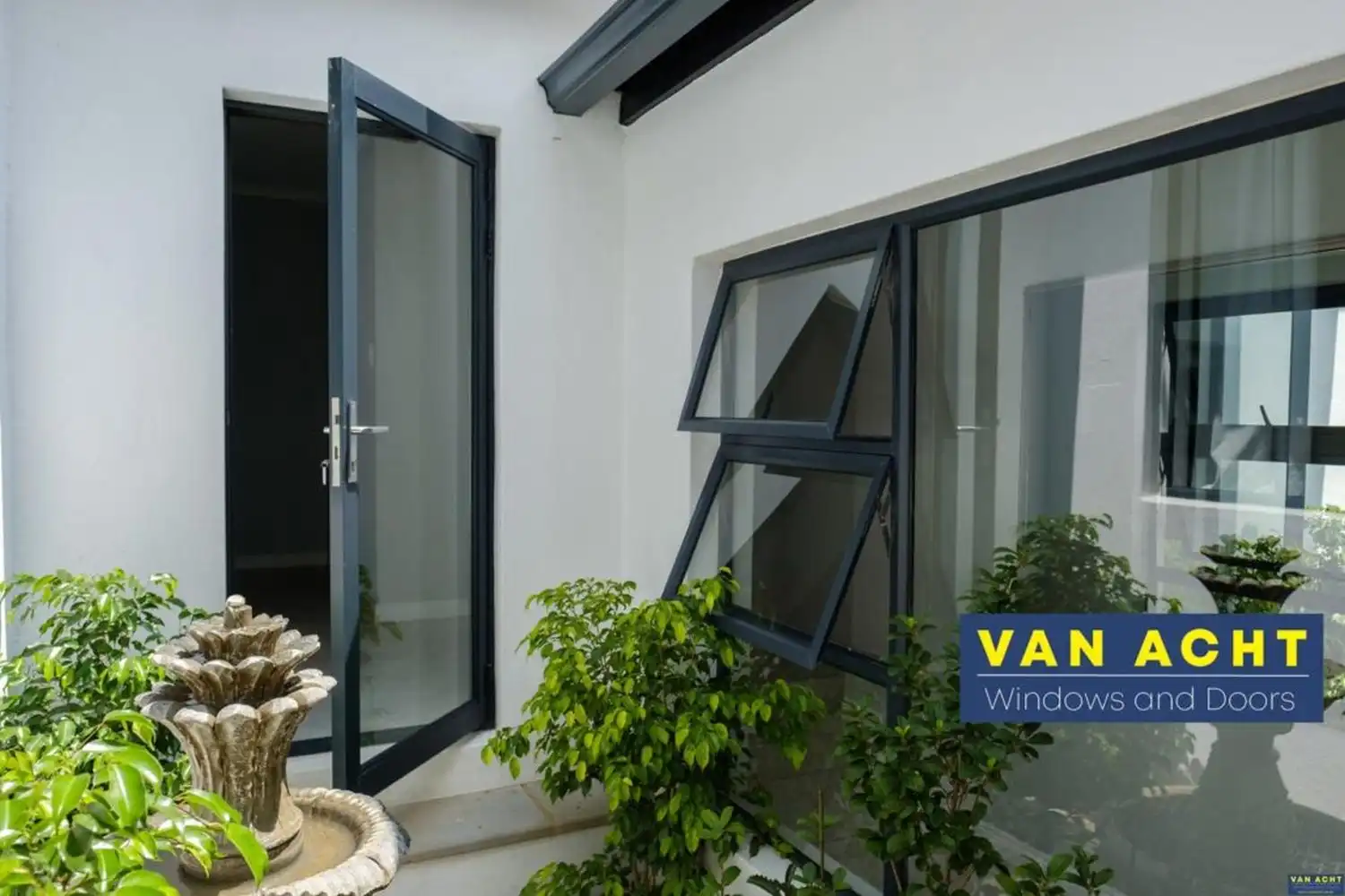 Van Acht aluminium hinged door and awning window in dark grey installed in a white rendered courtyard setting