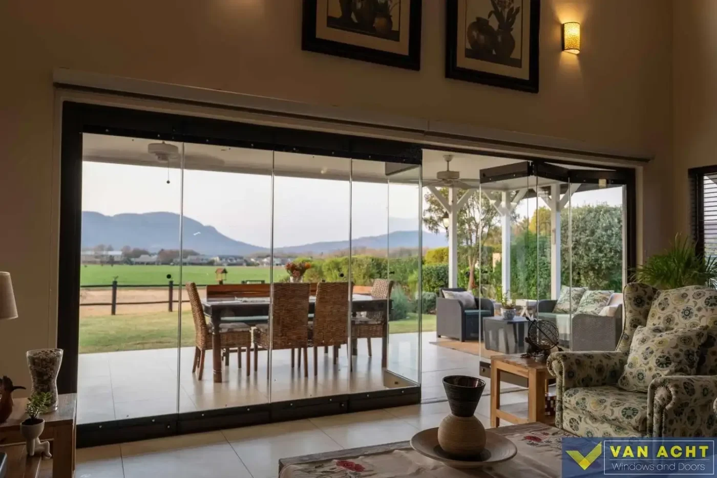van acht frameless glass folding doors open mountain view indoor outdoor Van Acht frameless glass folding doors fully open to a covered patio and mountain view in a South African home