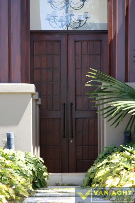 Tall dark wood double entrance door with square panel detailing and vertical bar handles, topped by a glass transom window.