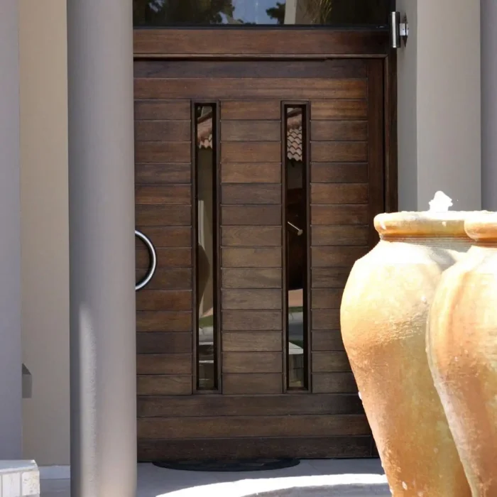 Close-up of a dark wood pivot entrance door with narrow vertical glass strips and a ring pull handle