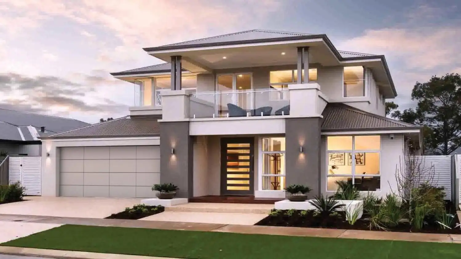 Light-toned aluminium composite panel garage door on a two-storey modern home with a covered balcony, photographed at dusk