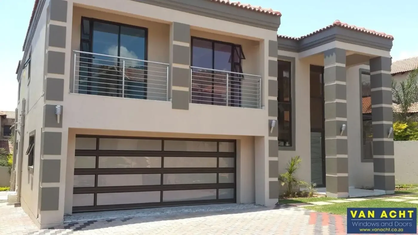 van acht aluminium glazed sectional garage door bronze frame double storey home Dark bronze-framed aluminium sectional garage door with glazed panels below a balcony on a double-storey home.